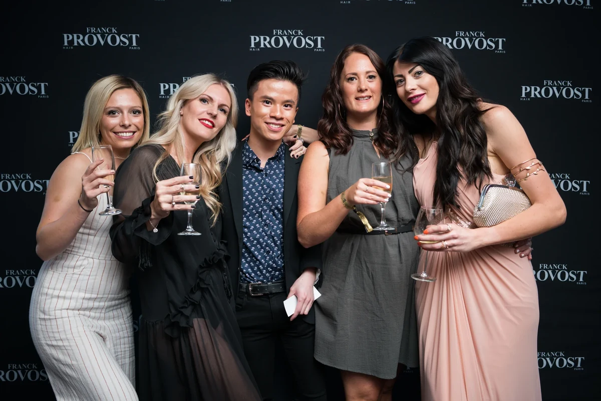 Groupe d'invités souriants avec une coupe de champagne devant le photocall de marque lors d'une soirée d'entreprise à Marseille